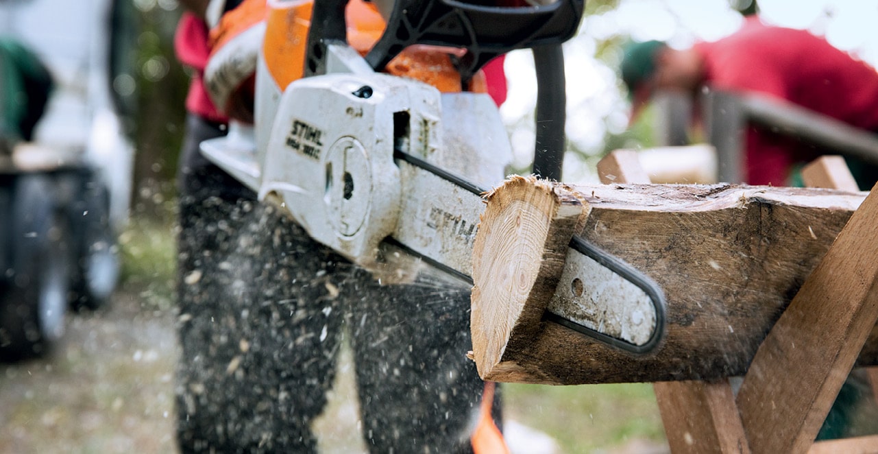 STIHL petrol chainsaw cutting a log on a sawhorse with wood chips flying