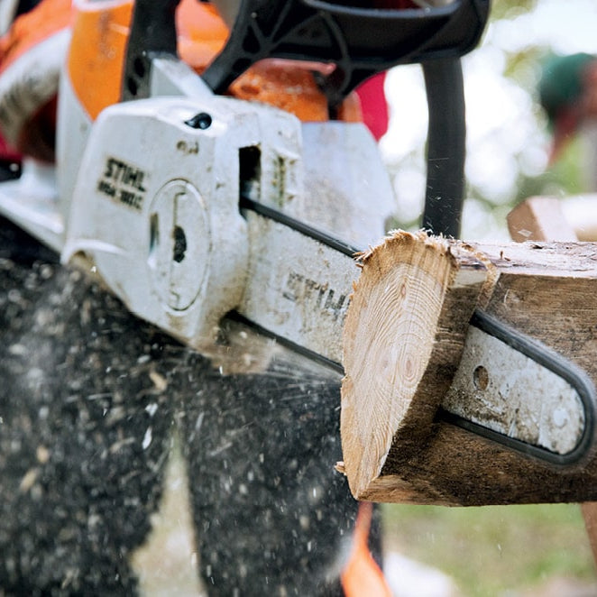 STIHL petrol chainsaw cutting a log on a sawhorse with wood chips flying