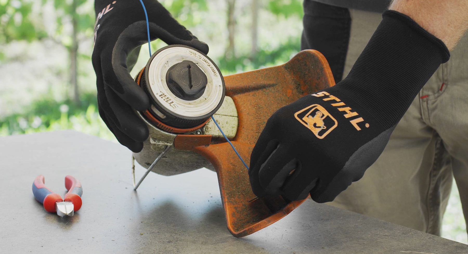 Gloved hands replacing cutting line in a STIHL FSA 57 grass trimmer head on a workbench