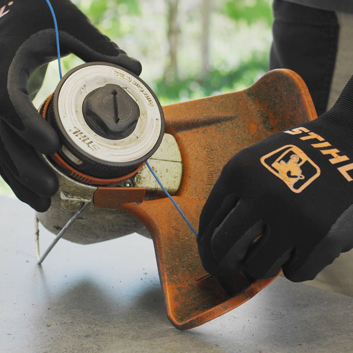 Gloved hands replacing cutting line in a STIHL FSA 57 grass trimmer head on a workbench